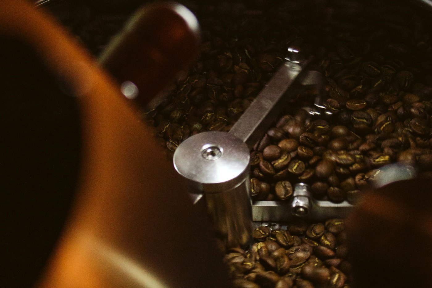Close-up inside a drum roaster — the steel agitator paddle sweeps through beans in low, warm lamp light